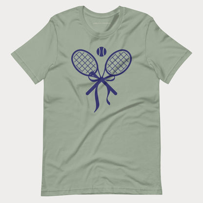 A sage green short-sleeve crewneck tennis t-shirt featuring a dark blue graphic of two crossed tennis rackets tied with a bow, with a tennis ball above them.