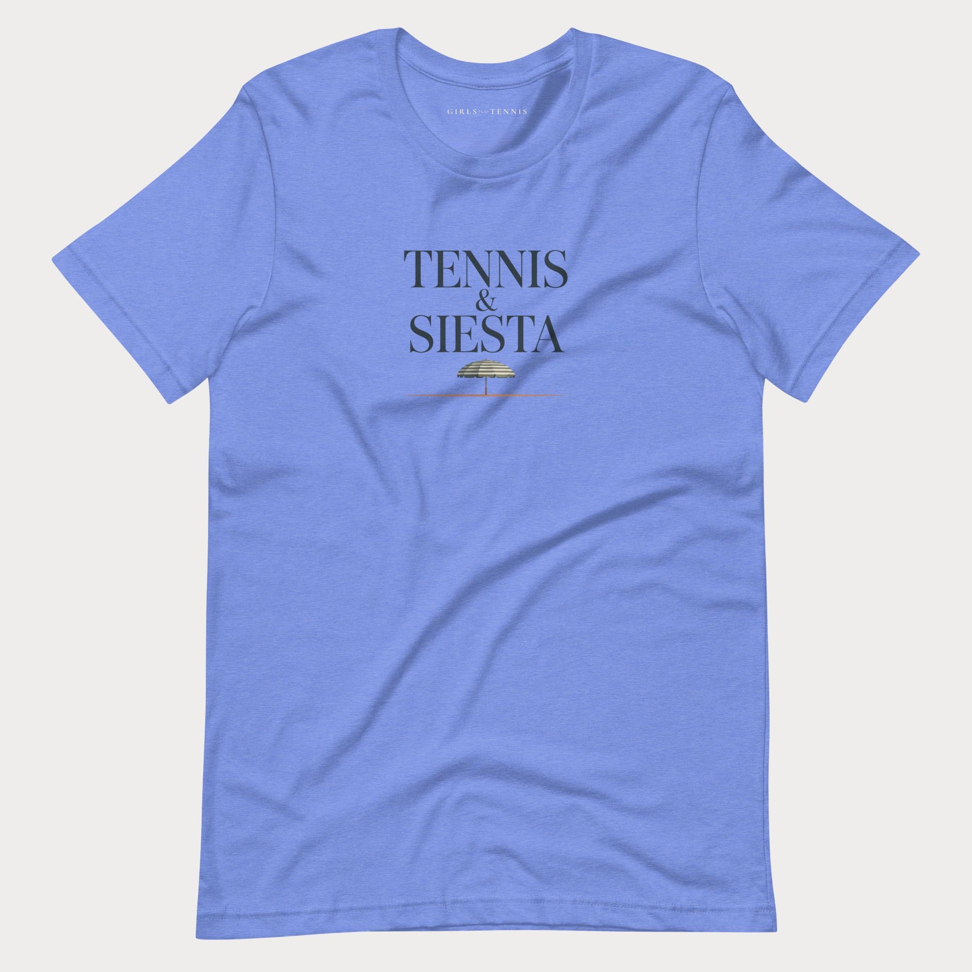 A heather blue short-sleeve women's lifestyle t-shirt with 'TENNIS & SIESTA' printed in navy on the chest, accompanied by a small gold graphic, displayed flat against a light gray background.