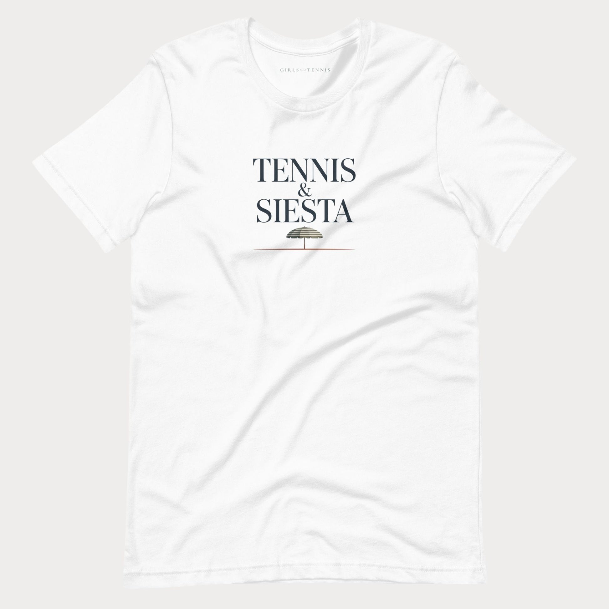 A white short-sleeve crewneck women's lifestyle t-shirt with 'TENNIS & SIESTA' printed in black serif letters on the chest, with a small umbrella graphic underneath, shown against a light gray background.