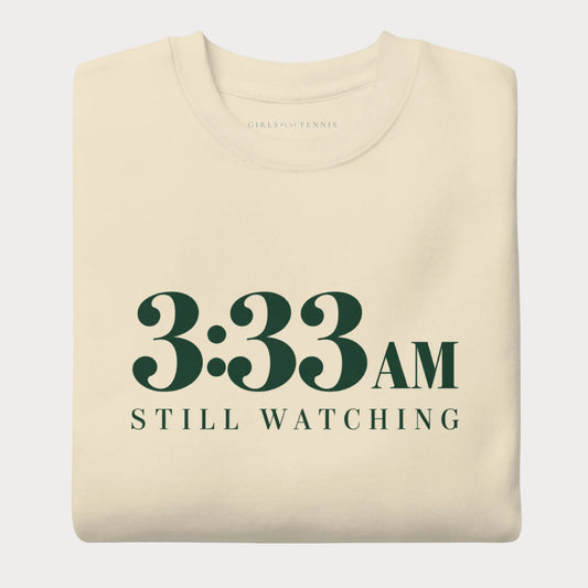 Folded bone 3:33 AM women's tennis crewneck sweatshirt with forest green lettering reading 3:33 AM above Still Watching