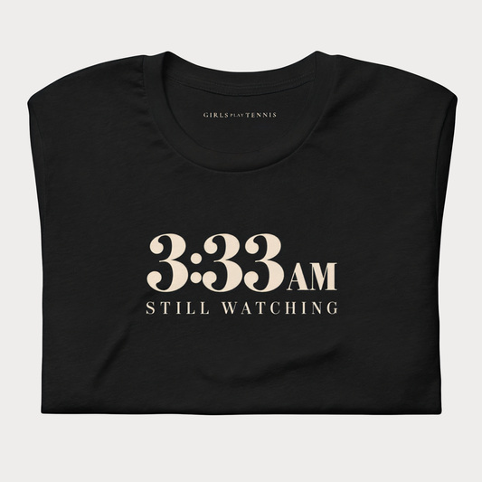 Folded black 3:33 AM women's tennis T-shirt with cream lettering reading 3:33 AM above Still Watching