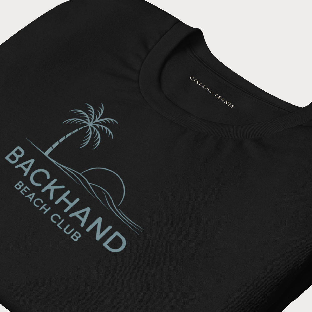 Close-up of the palm tree, sun and waves graphic on a black Backhand Beach Club women's tennis T-shirt