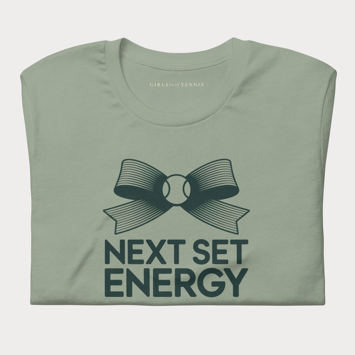 Folded sage green Next Set Energy women's tennis T-shirt with a bow around a tennis ball above bold lettering