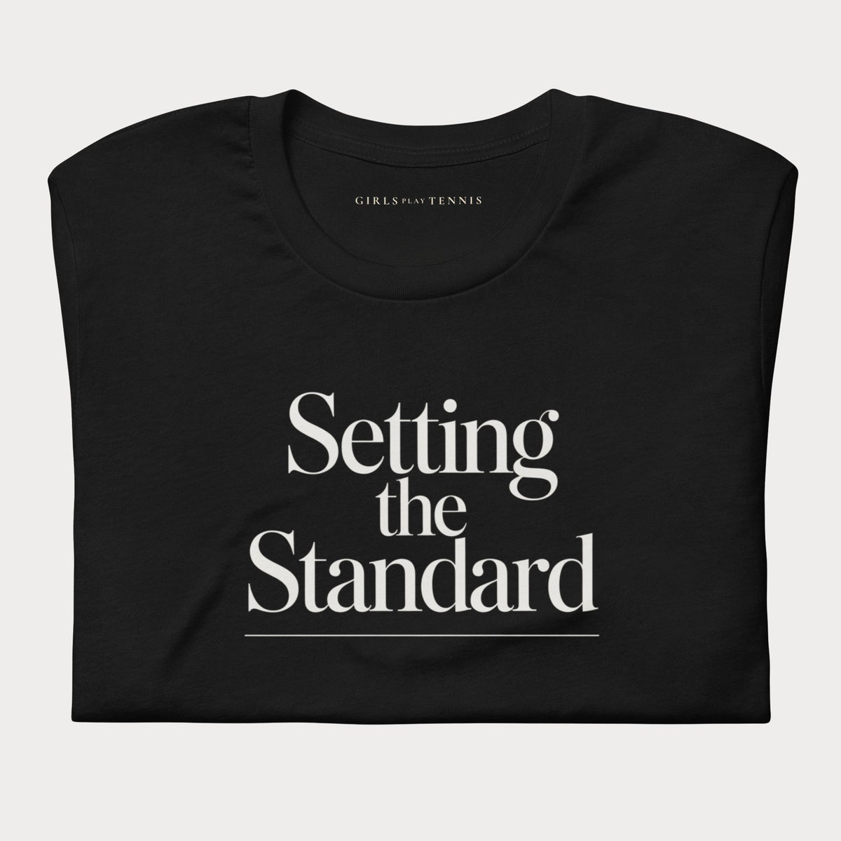 Folded black Setting the Standard women's tennis T-shirt with stacked serif lettering and a thin underline