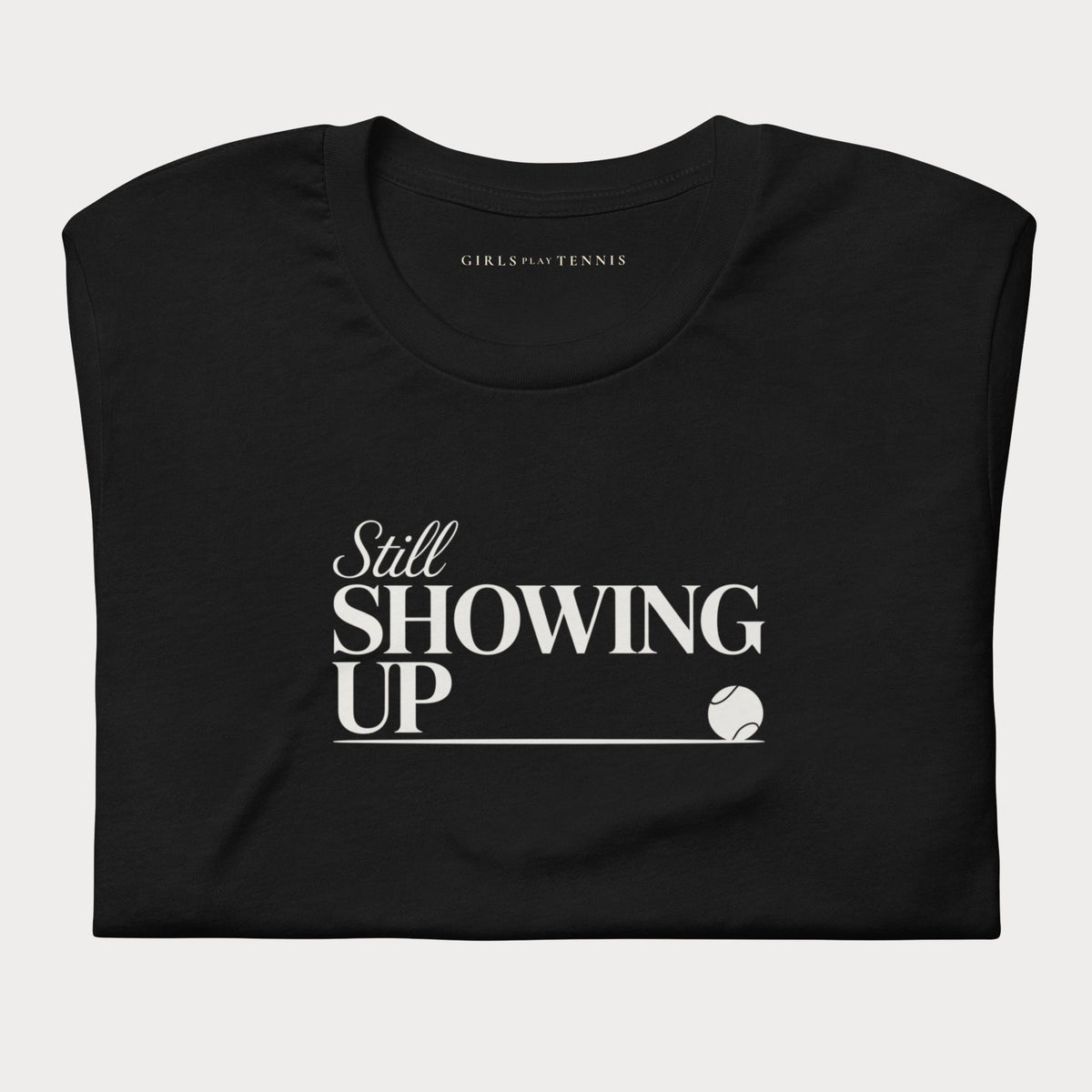 Folded black Still Showing Up women's tennis T-shirt with white lettering and a progress line ending in a tennis ball