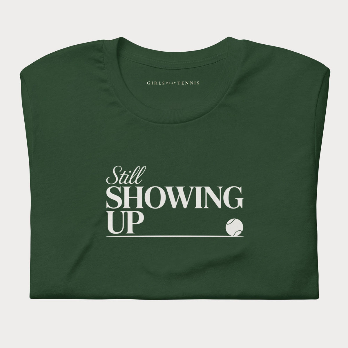 Folded forest green Still Showing Up women's tennis T-shirt with white lettering and a progress line ending in a tennis ball