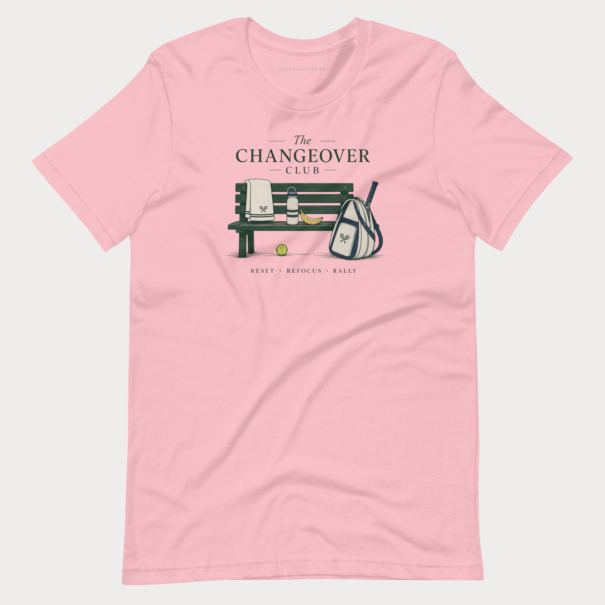 Pink The Changeover Club women's tennis T-shirt with a courtside bench, towel, racket bag and banana illustration